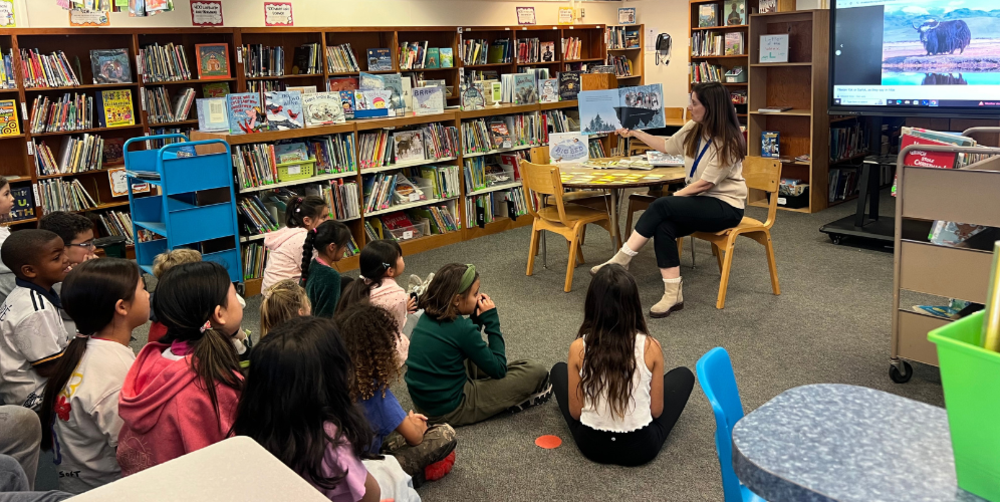 A woman reads to a group of children in a library filled with books.