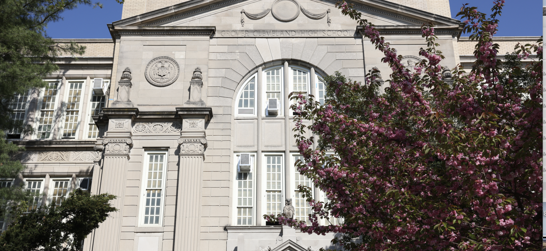 Historic building facade with decorative elements and blooming pink flowers.