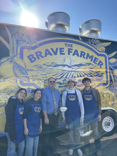 A group of five people in blue aprons standing in front of a colorful food truck.