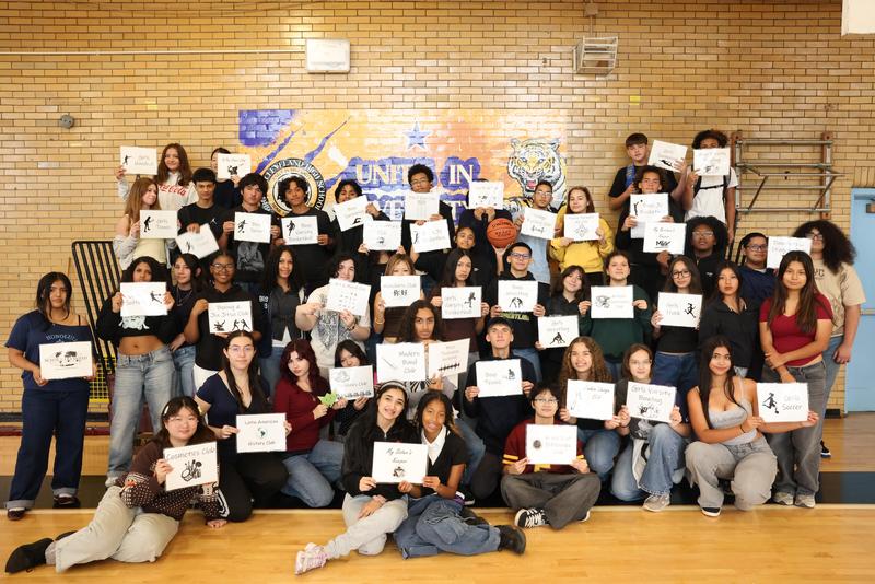 Students posing to the photo and holding their Club Name pages
