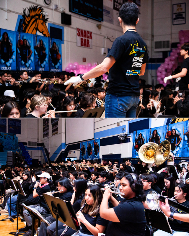 Conductor leads a large band performing in a gym with banners and students seated.