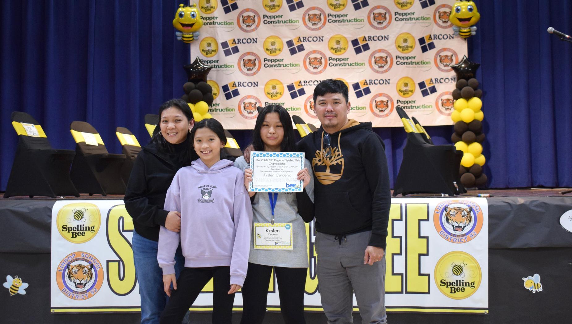 Four people pose with a certificate at a spelling bee event.