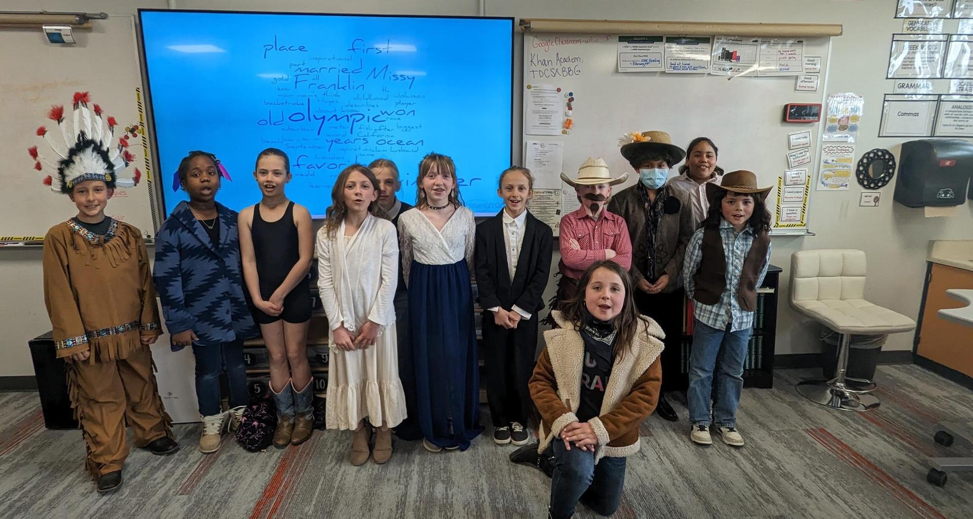 A group of children in costumes for a presentation, with a digital screen behind them.