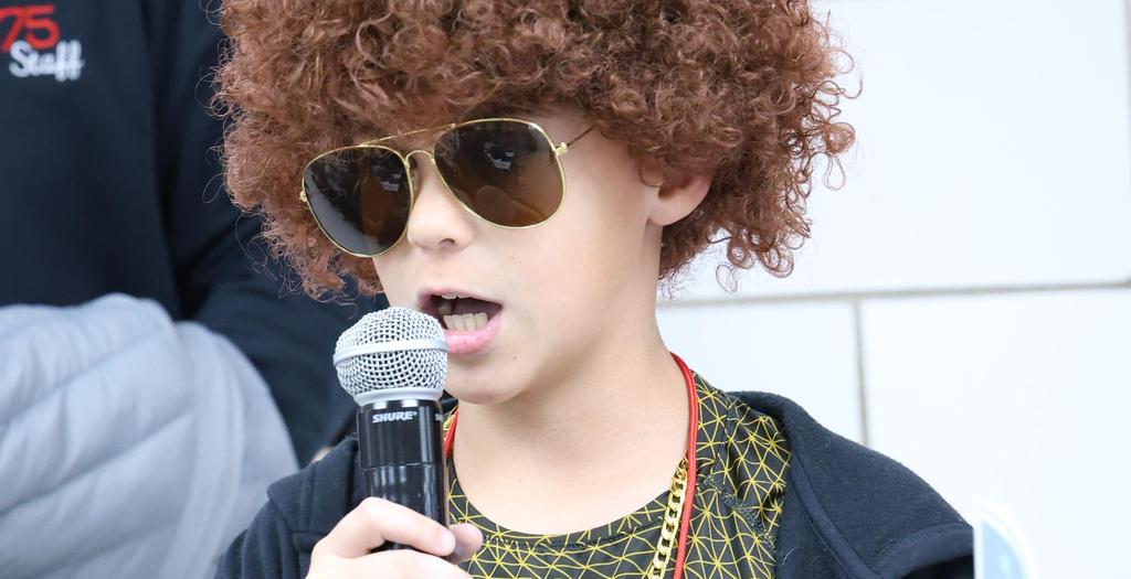 Boy holding a microphone, wearing a brown wig.