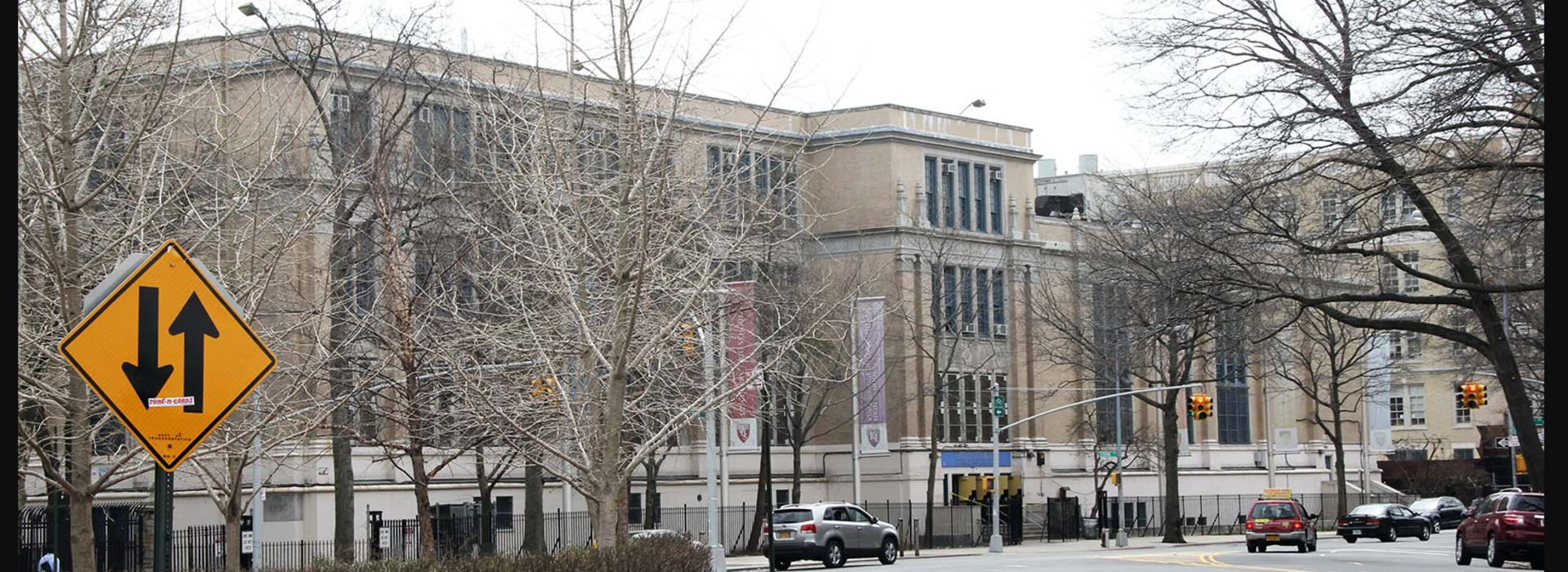 Urban street scene featuring a school building and a road sign indicating a one-way street.
