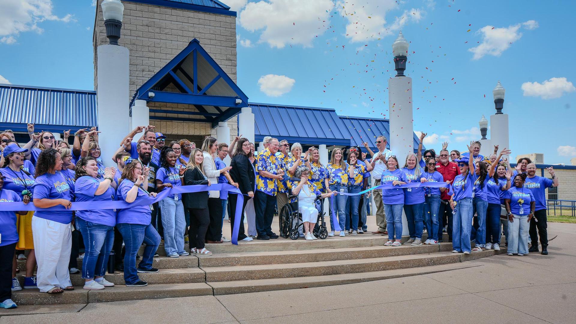 Group of people celebrating and cutting a ribbon outside a building.