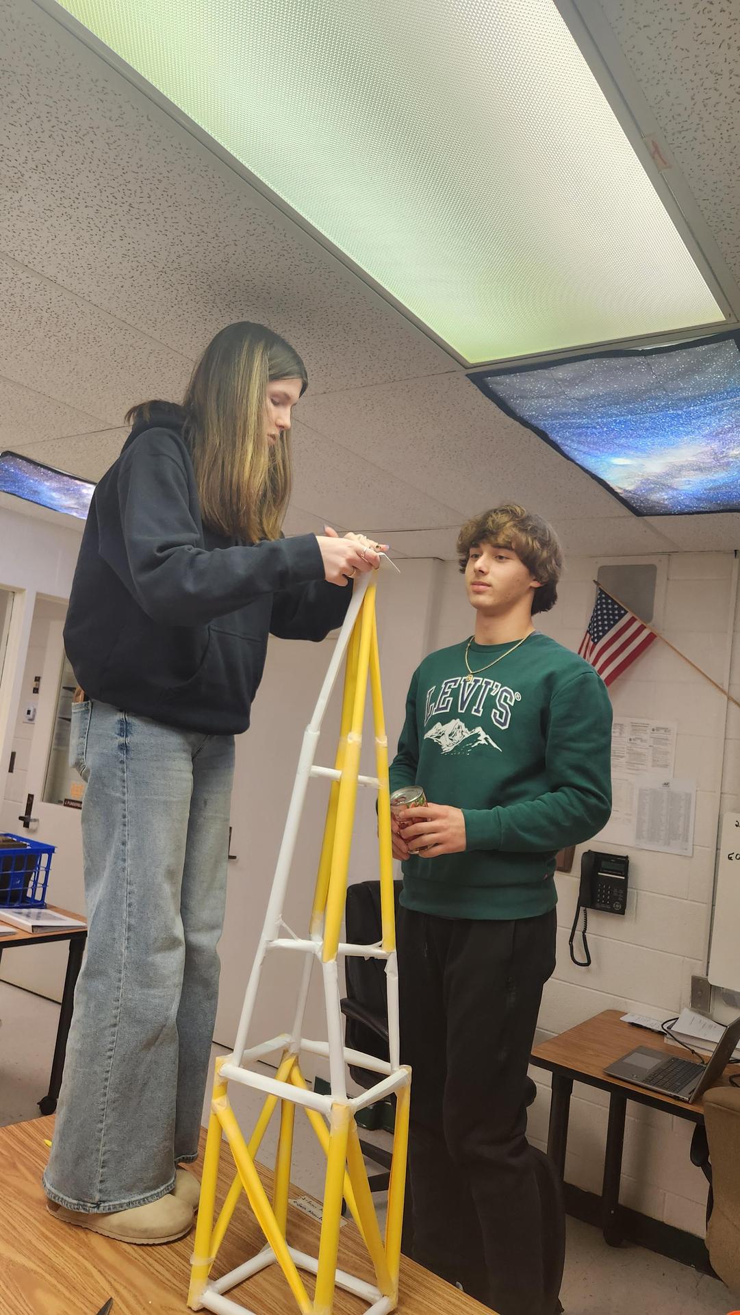 Students building a yellow and white tower structure in a classroom.