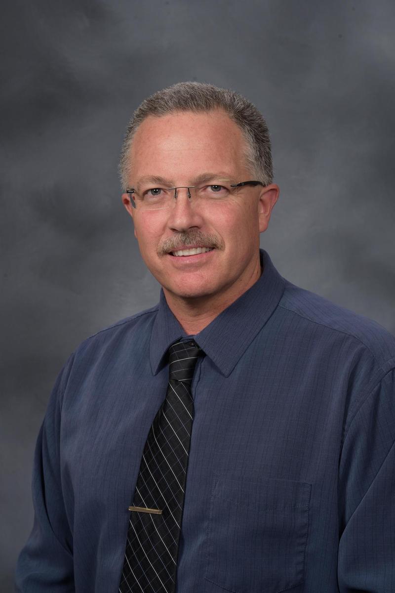 Sanchez in a blue shirt and tie, with a gray peppered mustache.