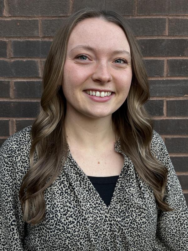 Young woman with long hair smiling against a brick wall.