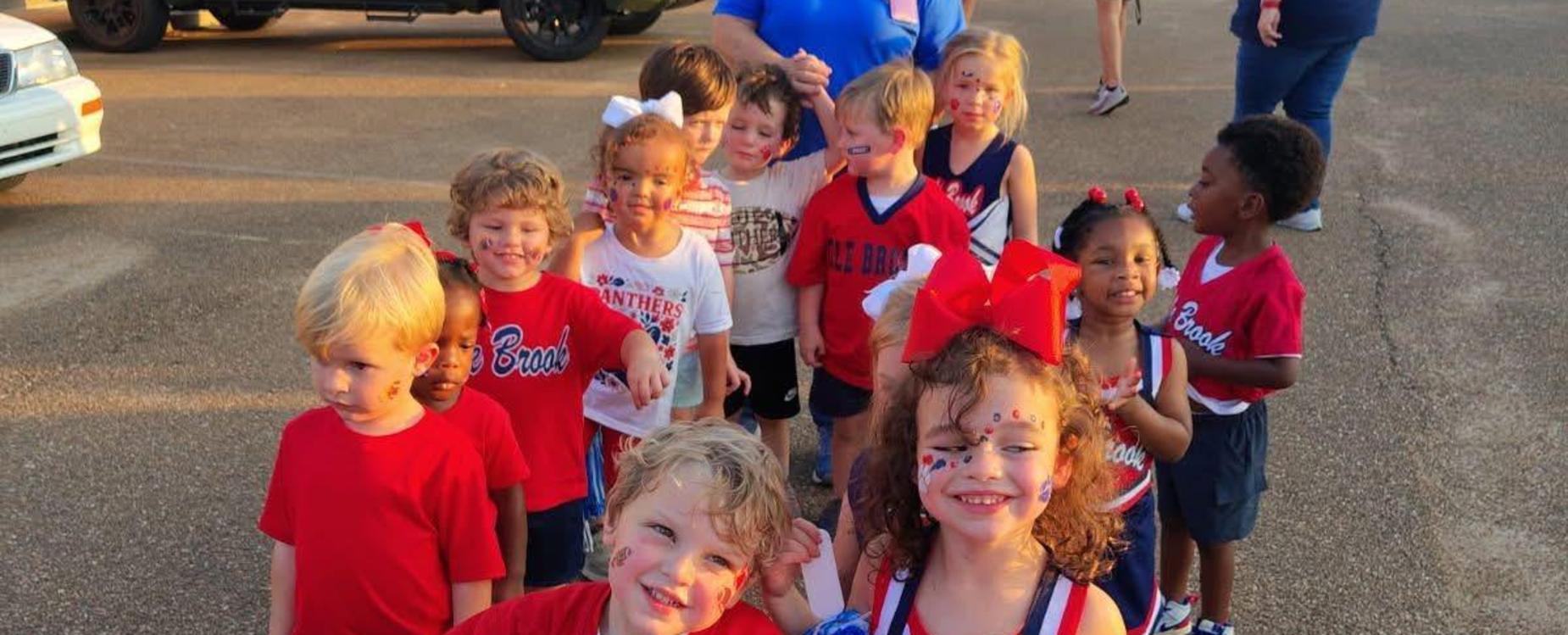 Cheerful group of children in red and blue outfits, celebrating with pom poms and a banner.