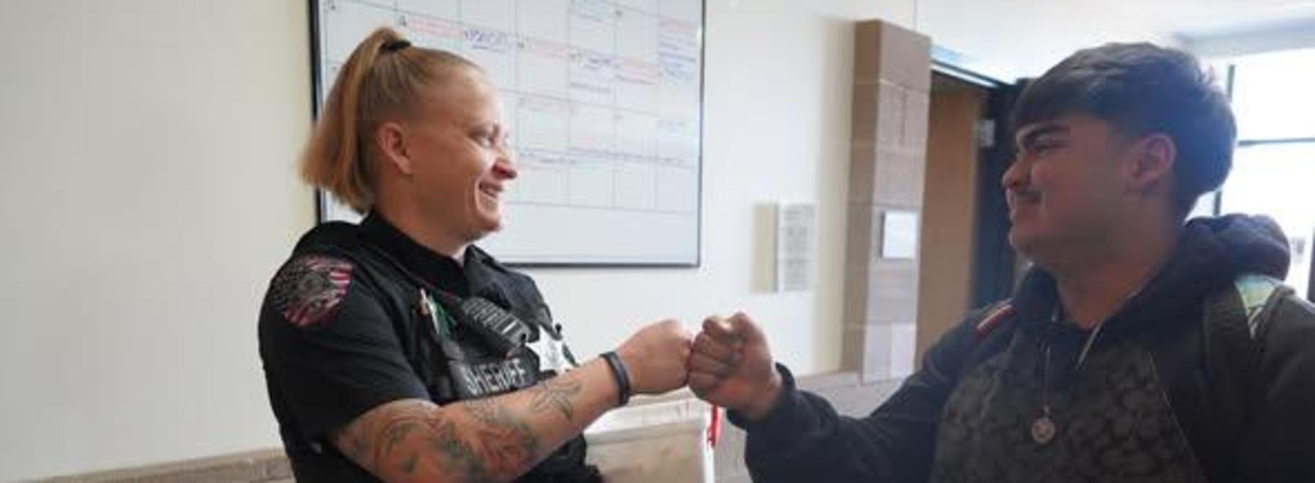 Two people fist bumping, one wearing a police uniform holding a container.