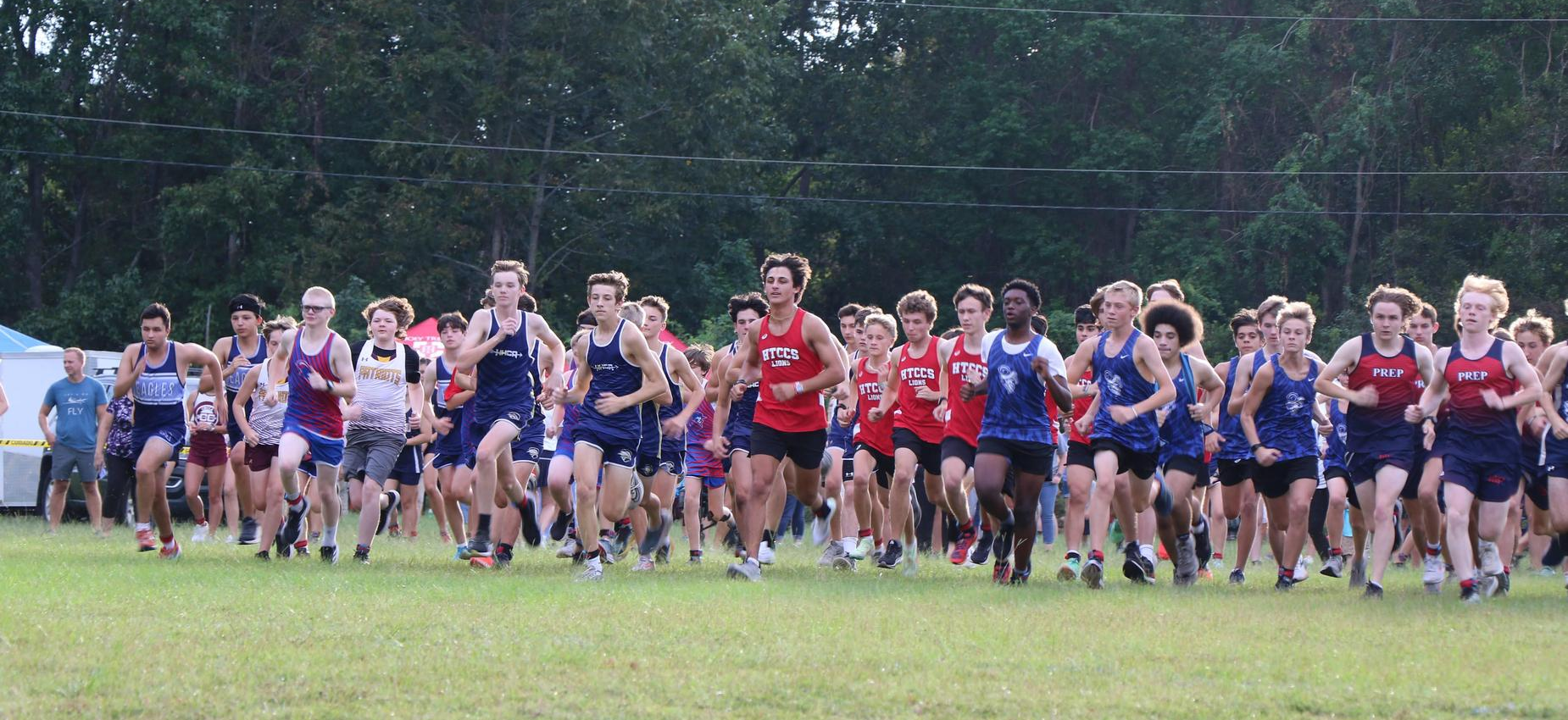 A large group of young male athletes running in a cross-country race.