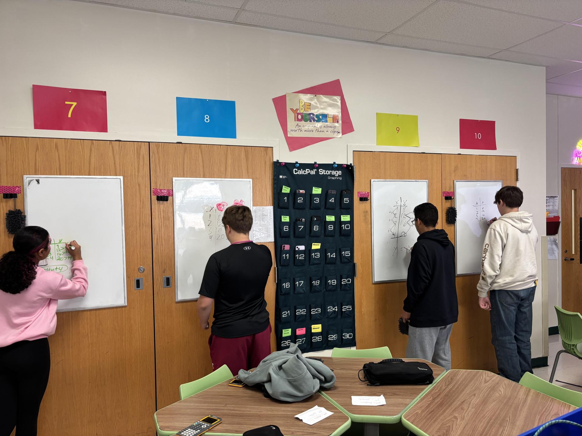 Students collaborating on whiteboards in a classroom environment.