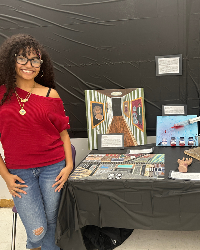 Student stands in front of their artwork at IB show