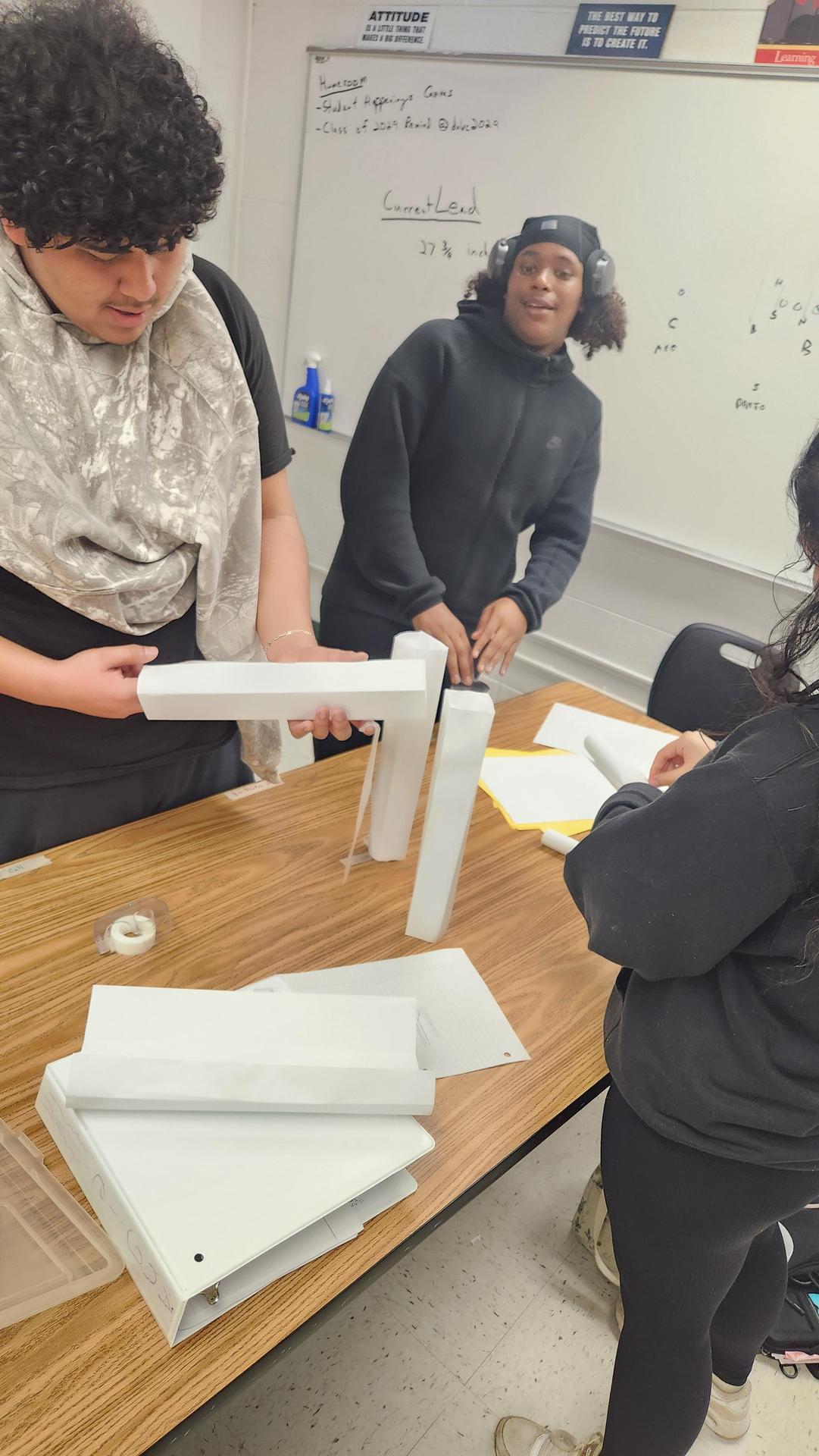 Students assembling a project at a table with various supplies.