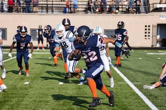 Football player in a blue uniform running with the ball while others chase.