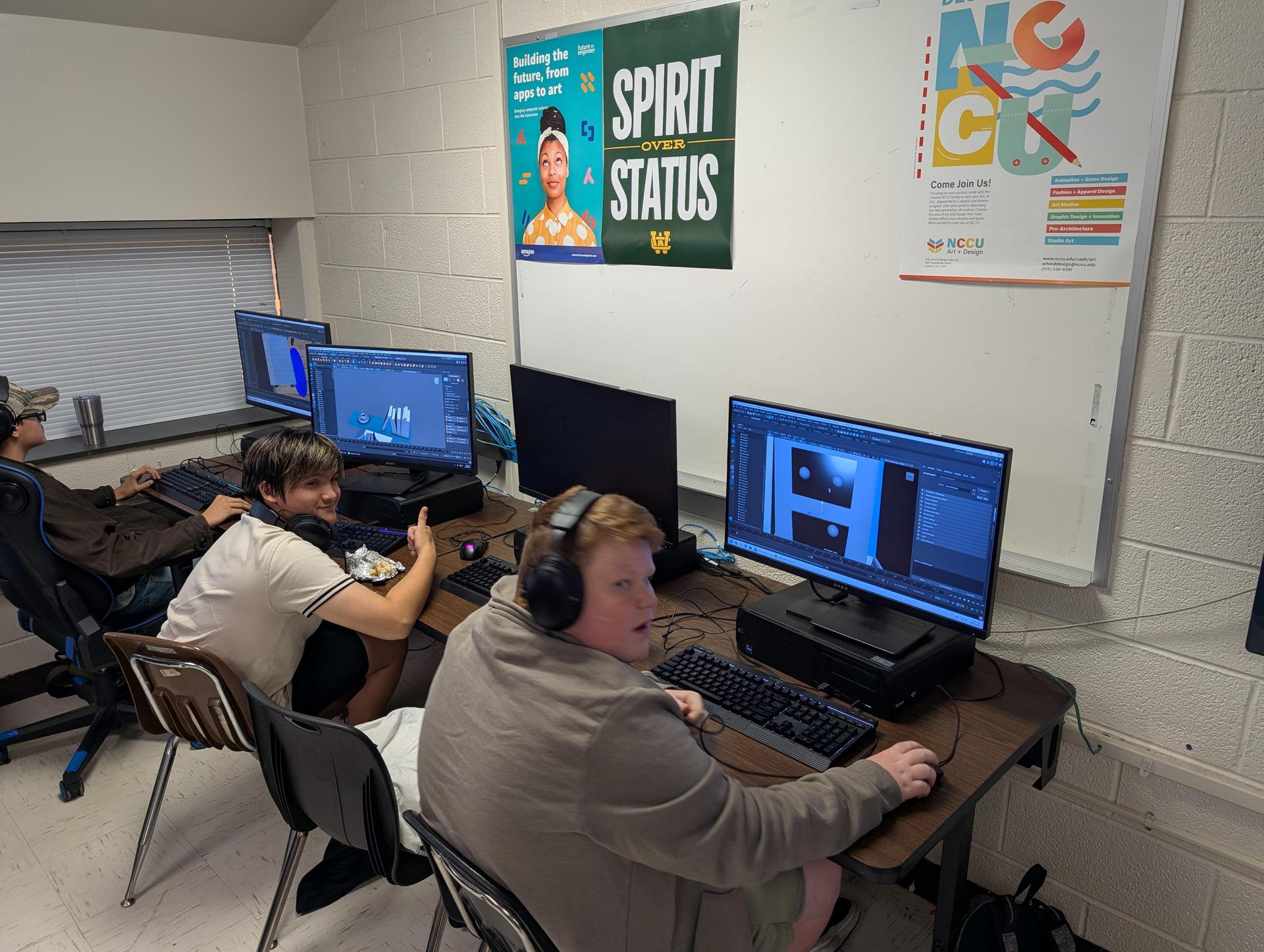 A student enjoying a snack while using a computer, with another working nearby in class.
