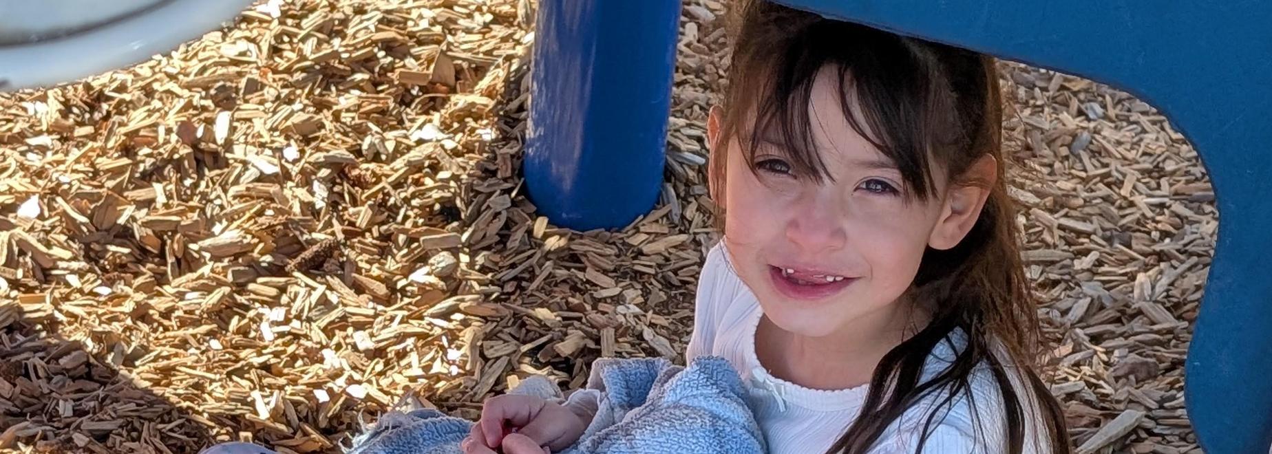 Girl sitting on wood chips with a blanket.
