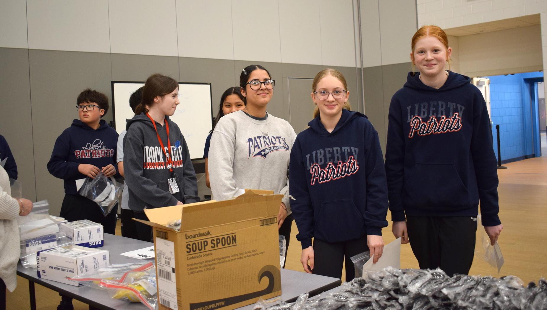 A group of teenagers gathered, wearing school hoodies, in a large open space.