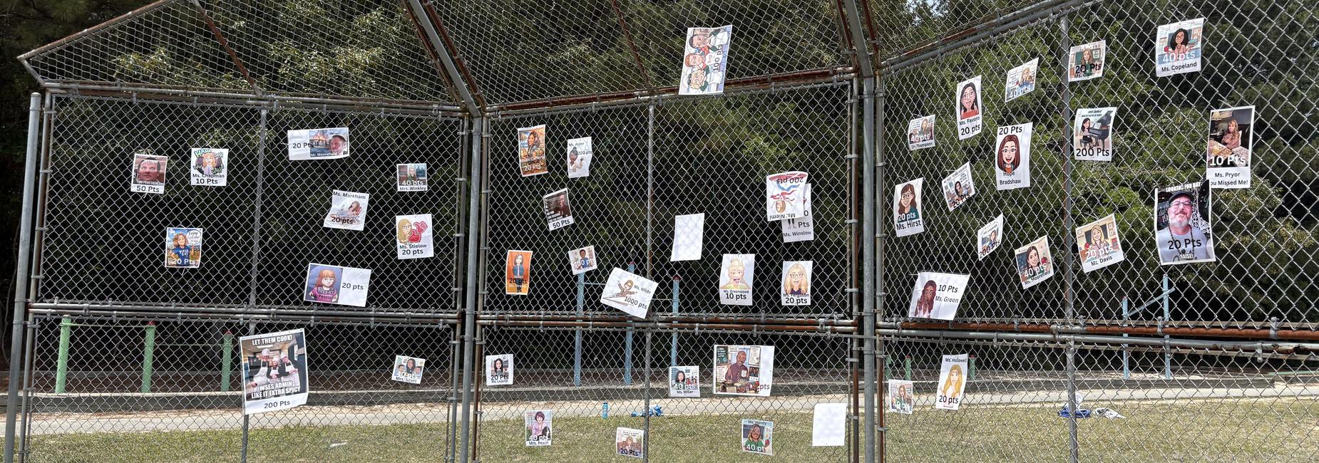 Dozens of posters with faces and text on a fenced area in a park.