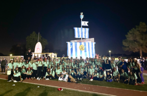 Students dressed in green posing in front of a decorated structure at night for school spirit.