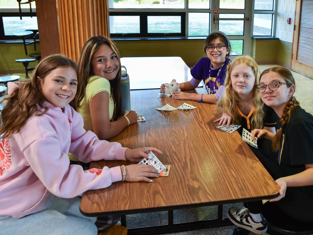 A group of students sitting at a table in the cafeteria participating in an after school club activity.