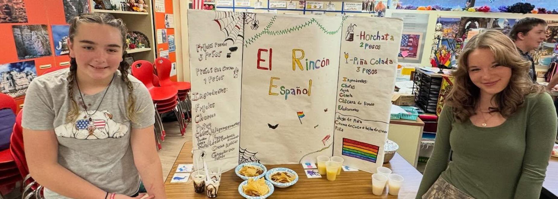 Two students presenting a project with food samples and a colorful display board in a classroom.