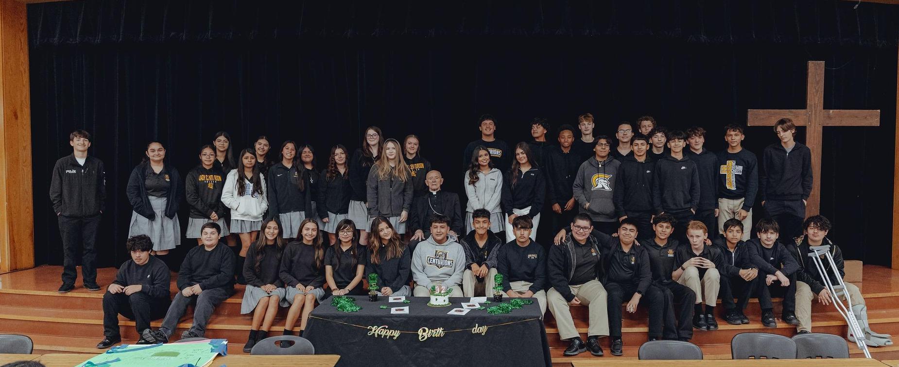 A group of students and teachers gathered for a birthday celebration in a school setting.