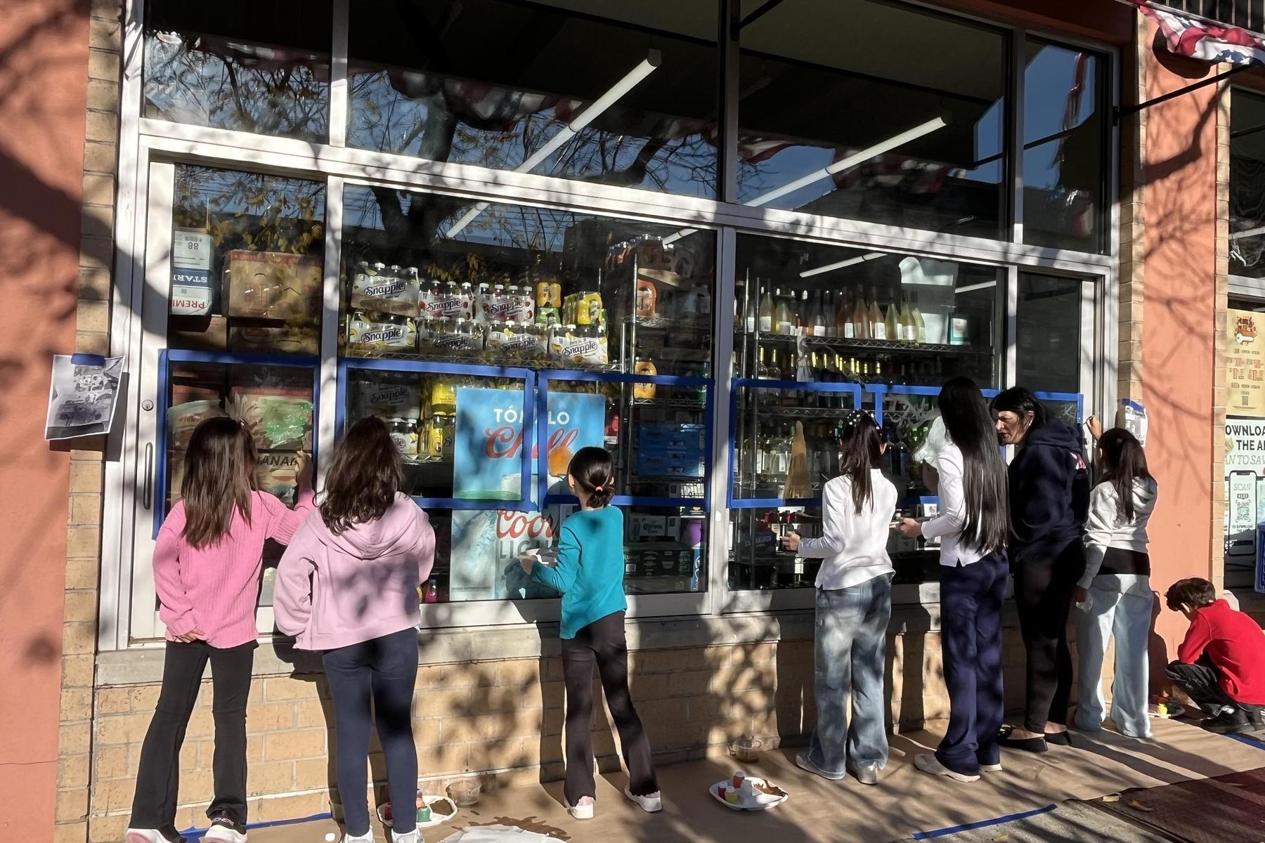 Group of children looking through a store window displaying various products.