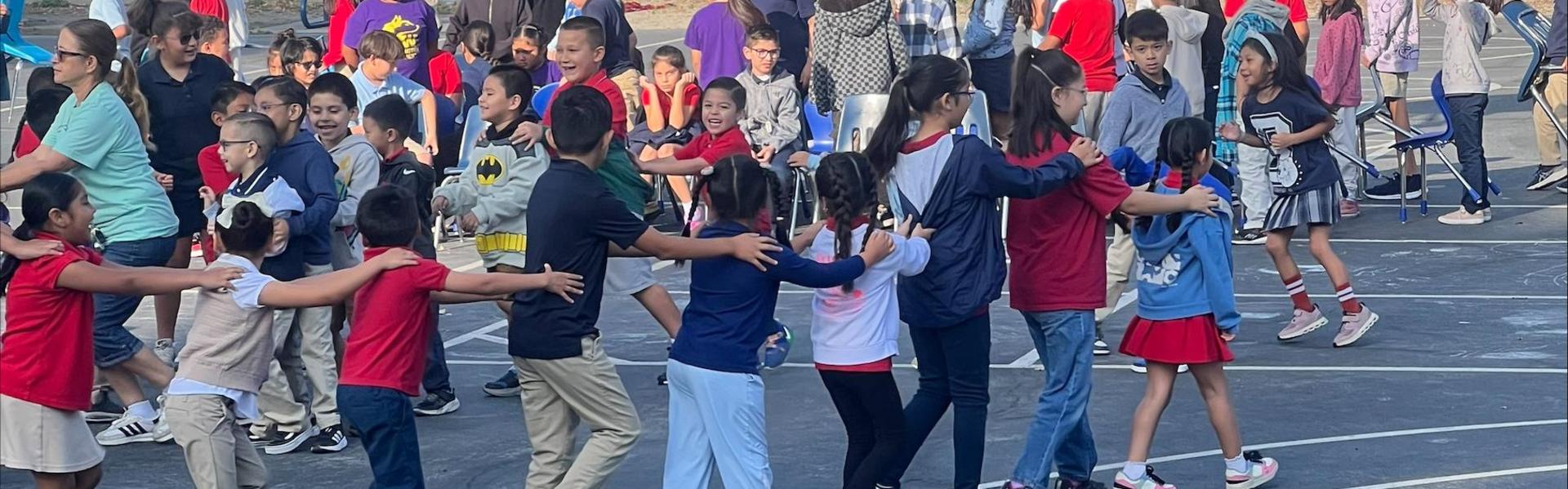 A line of children playing on a playground, holding onto each other's shoulders.