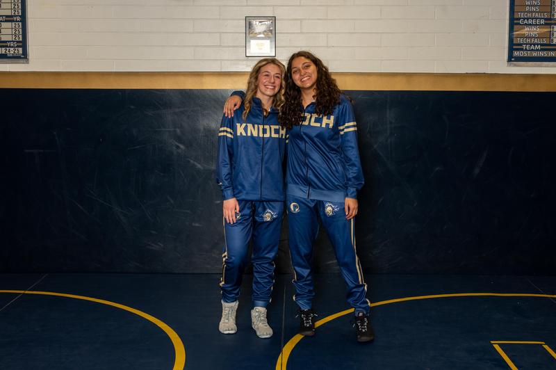 two high school girls dressed in wrestling attire smiling