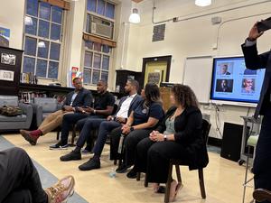 A panel discussion with five speakers seated in a library setting.