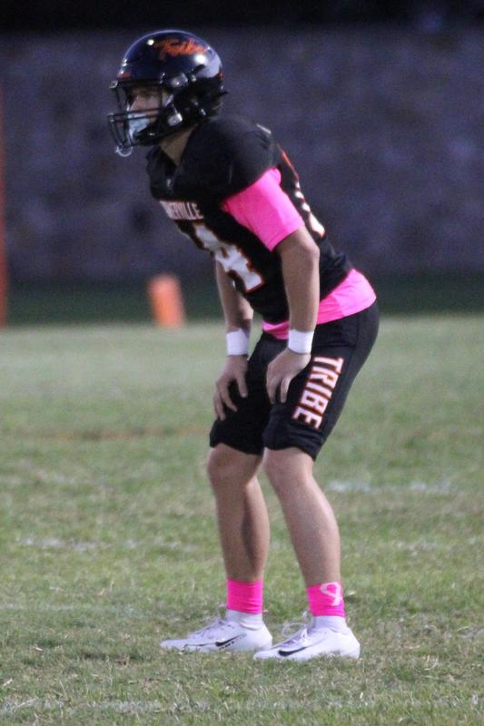 Football player in black jersey and pink sleeves preparing on the field.