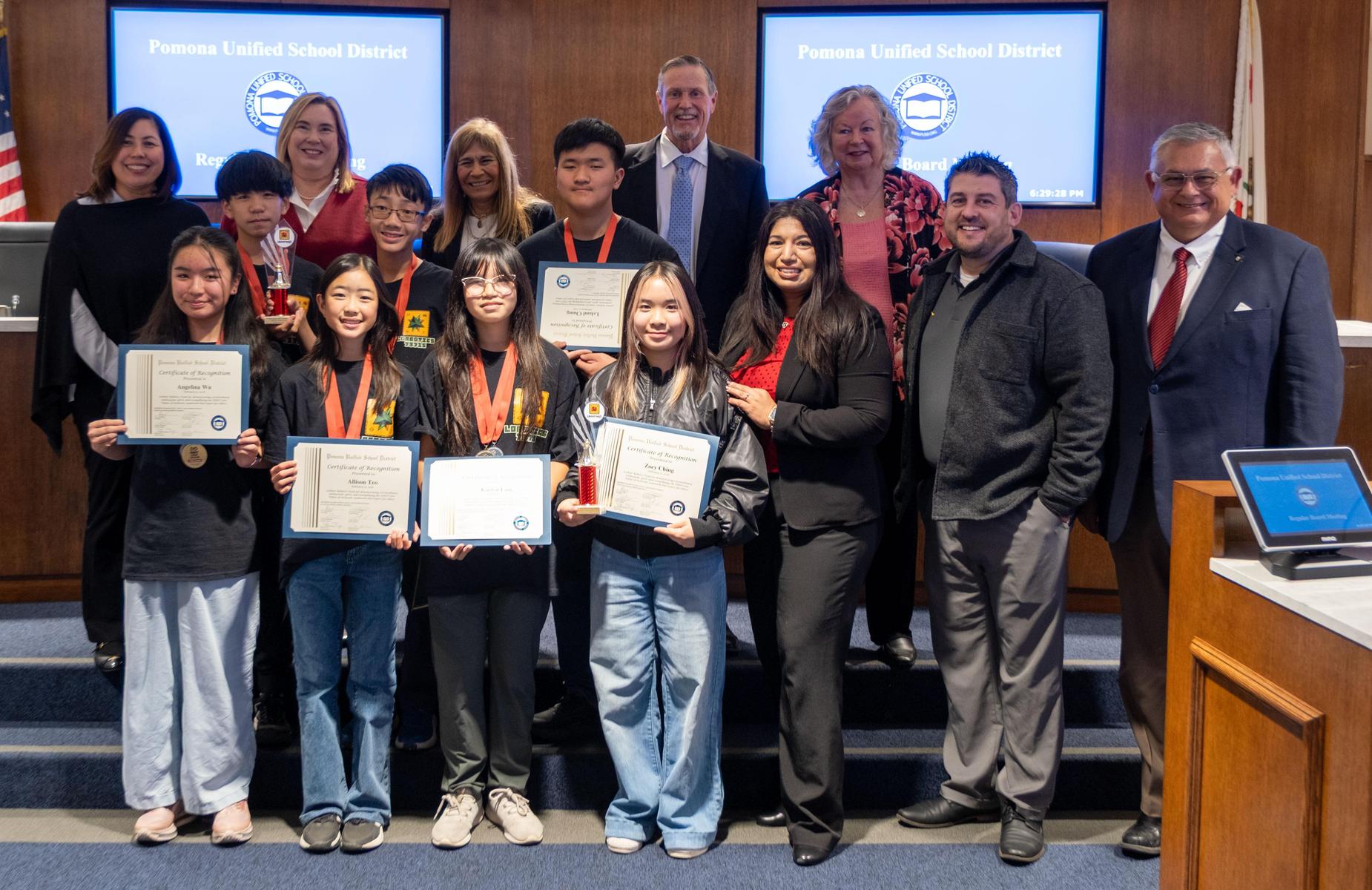 15 persons in school board room pose for photo with students