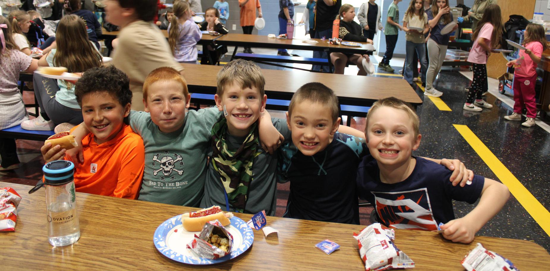 Five boys sit together at a table, enjoying snacks during a gathering.
