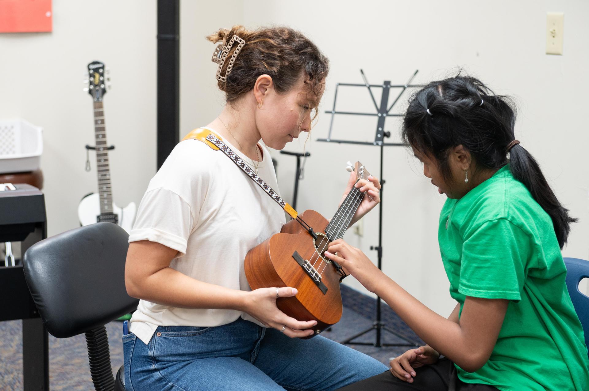 Teacher holding guitar while student touches strings.