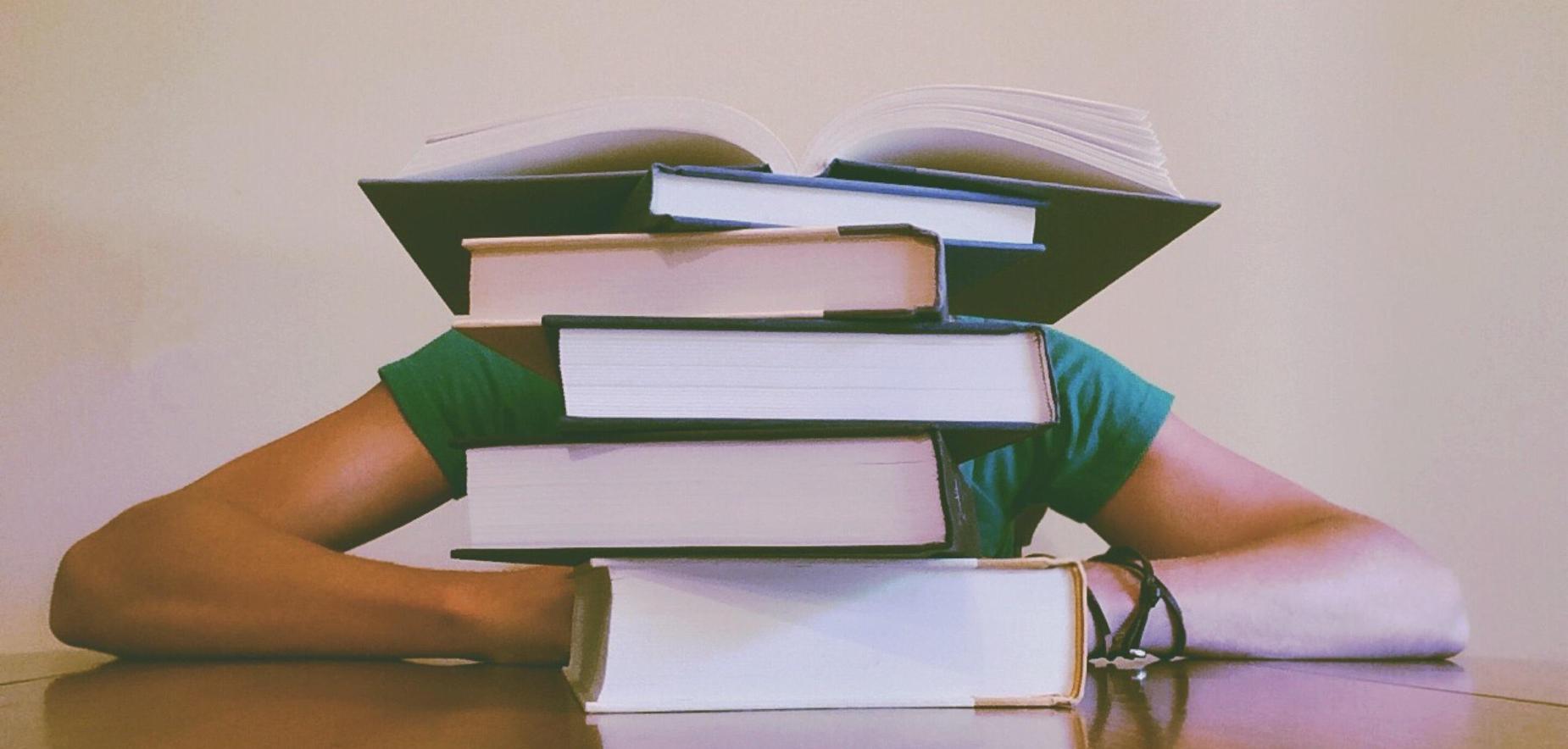 Student sitting behind stack of books