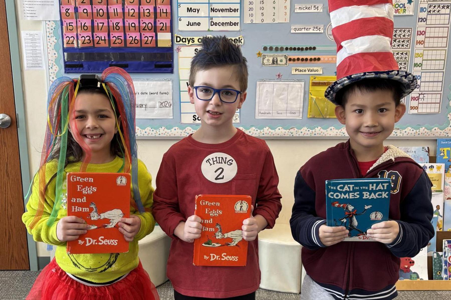 Three children dressed in costumes holding Dr. Seuss books in a classroom.