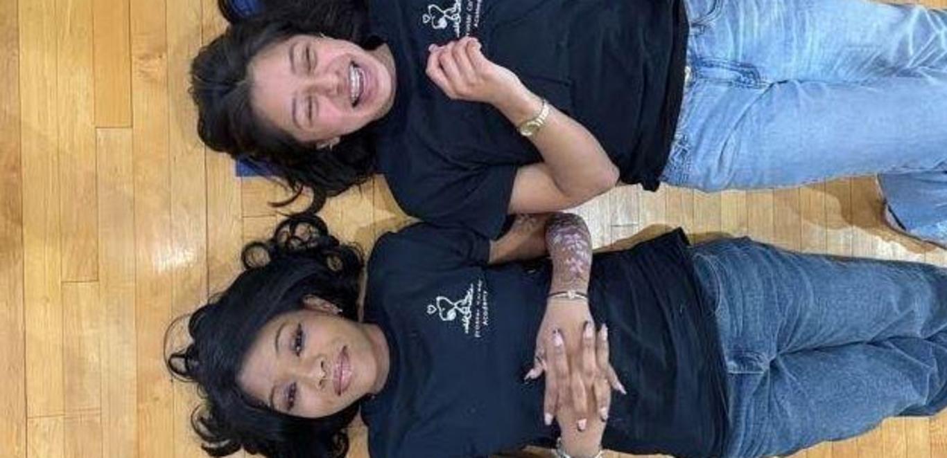 Two students from Armageddon lying on the floor laughing.