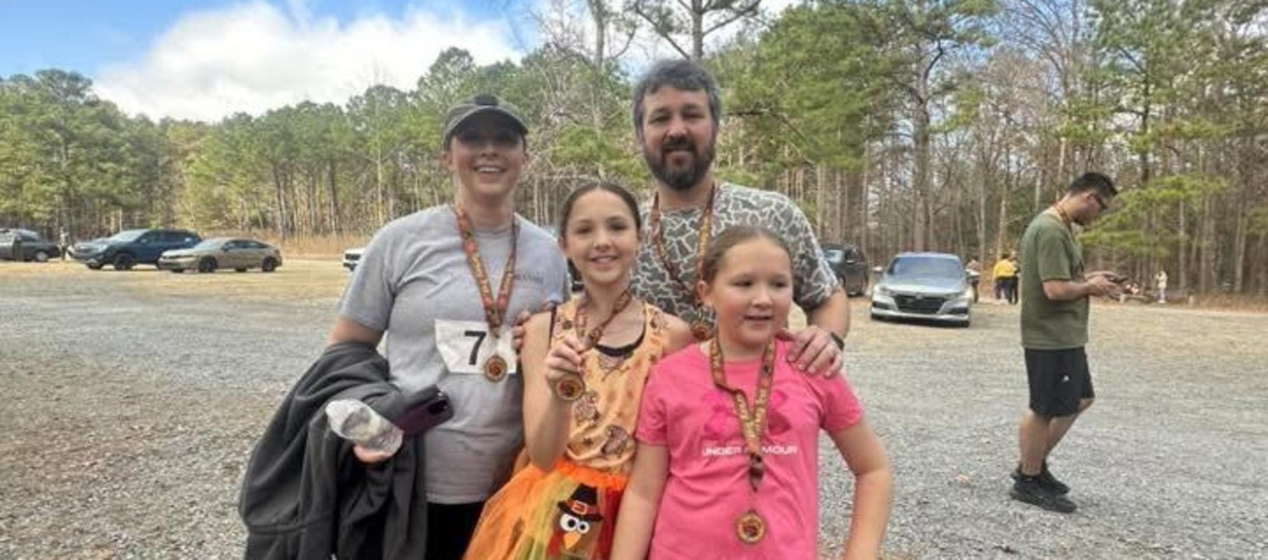 A family poses together after a run, wearing medals and smiling at the camera.