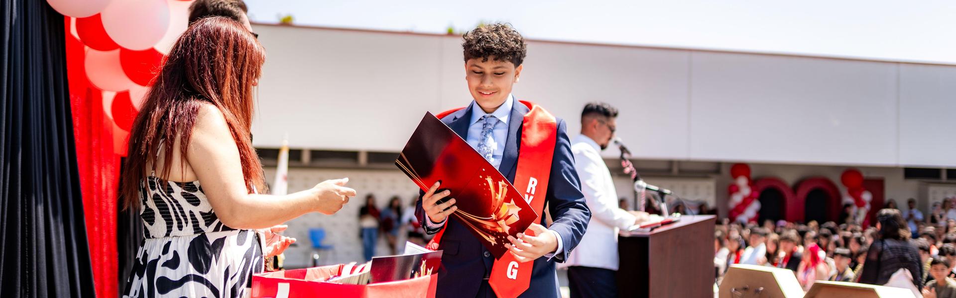 A student in a suit receiving a certificate at a graduation ceremony.