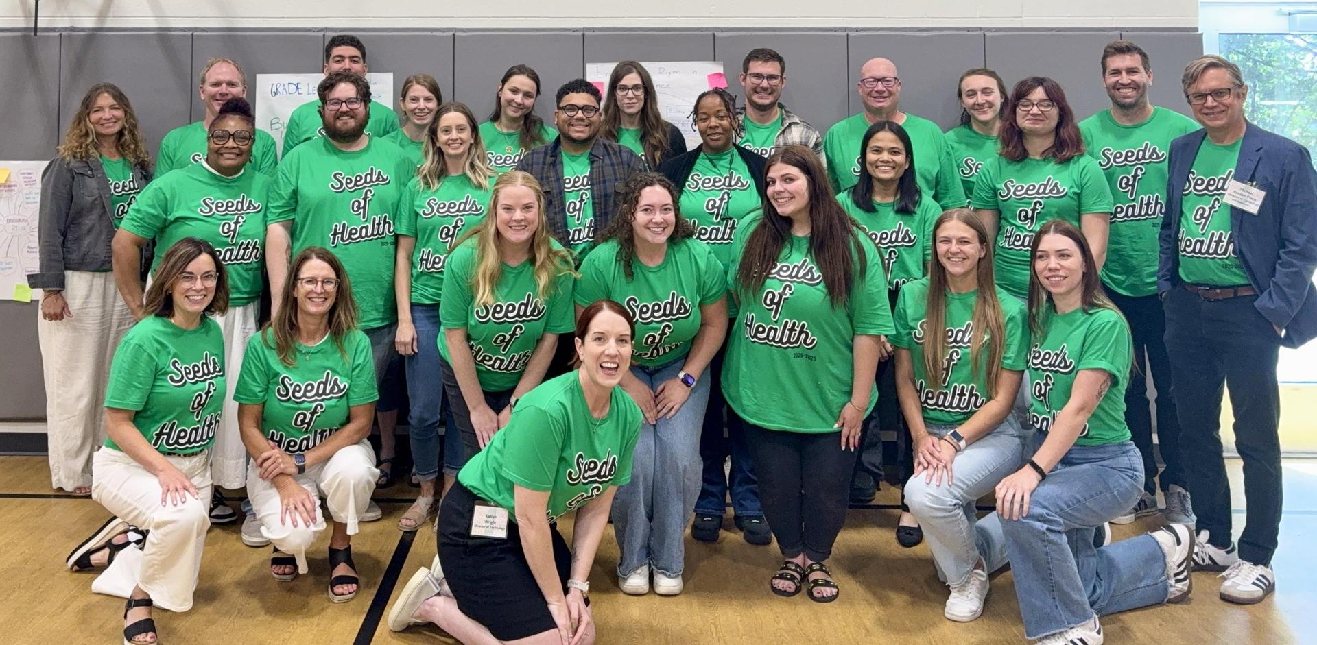 A large group of Seeds of Health staff smiling and wearing matching SOH shirts.