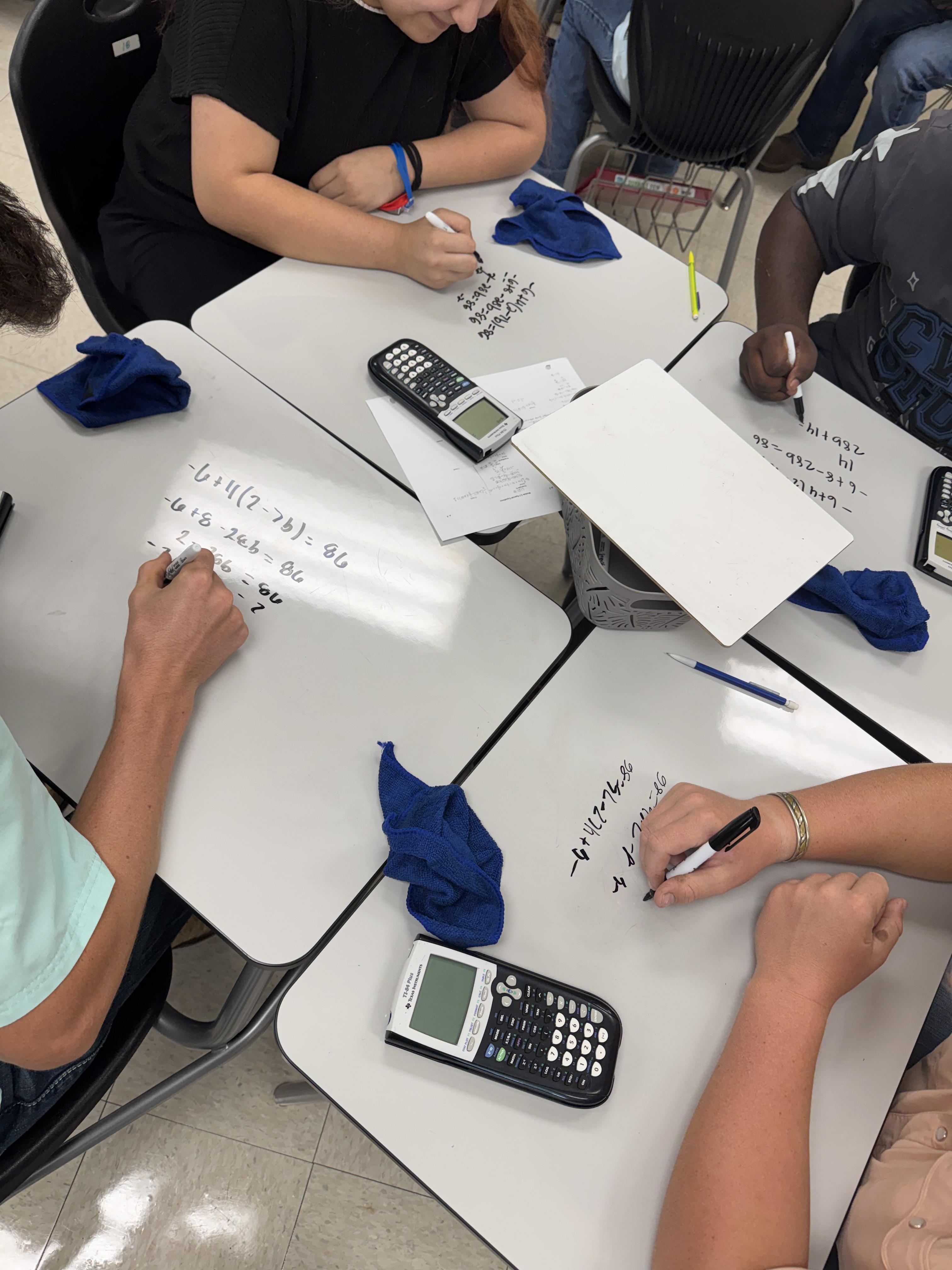 Students working equations on their dry-erase desk surface