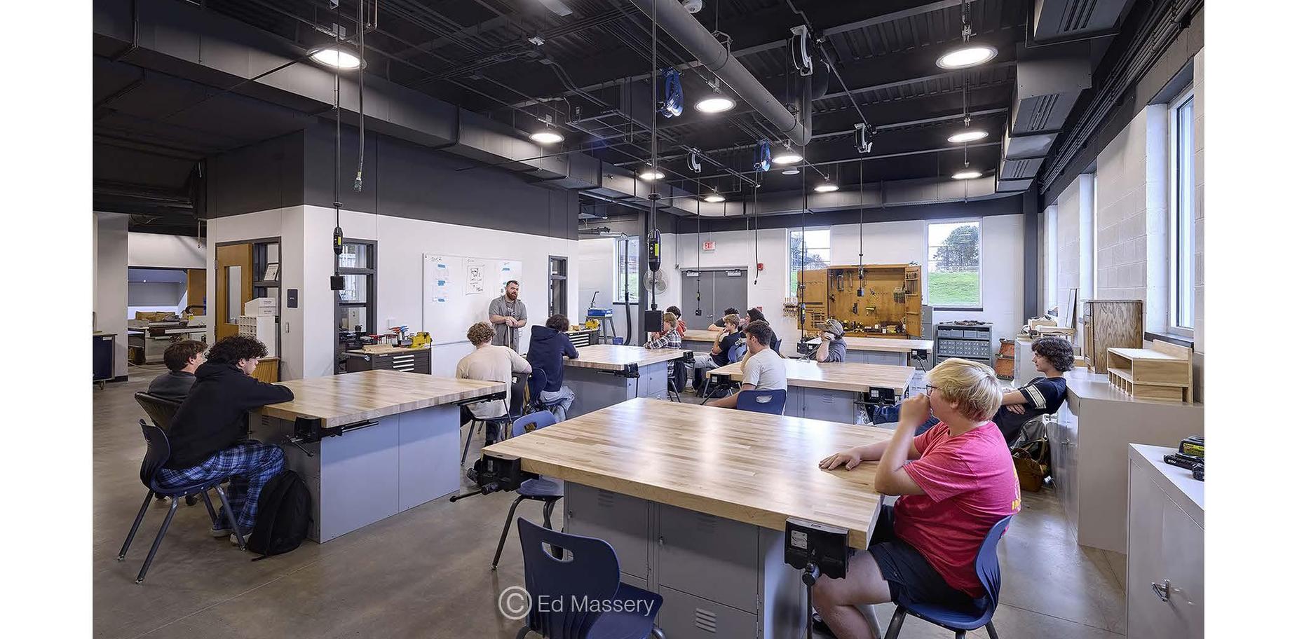 A classroom setting with students attentively listening to a teacher at the front.