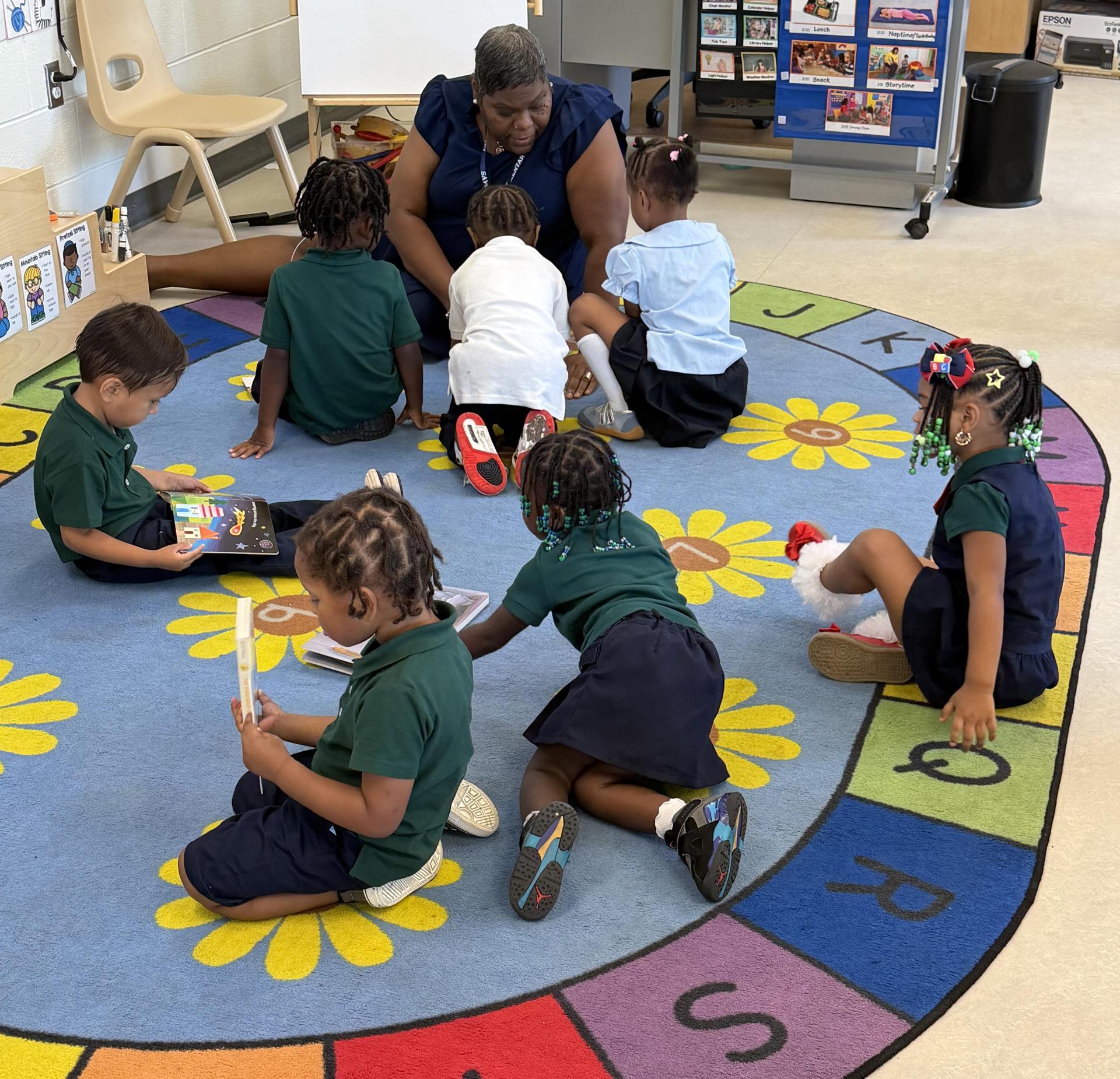 Children gathered on a colorful rug, reading and playing with an adult supervising.