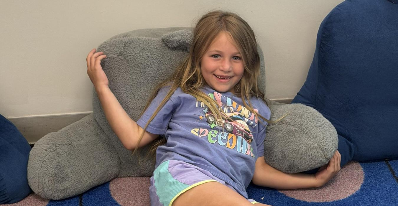 A girl in casual clothes sitting on a large, soft cushion.