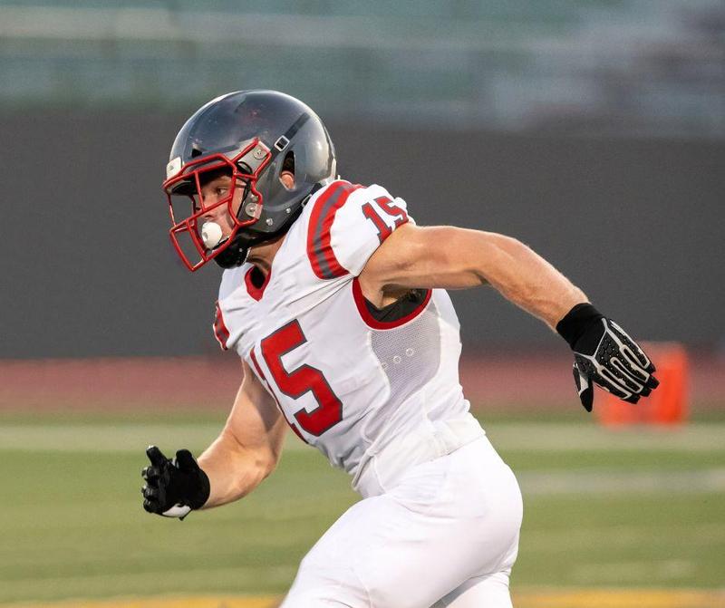 Football player in motion, wearing a white uniform and a red helmet.