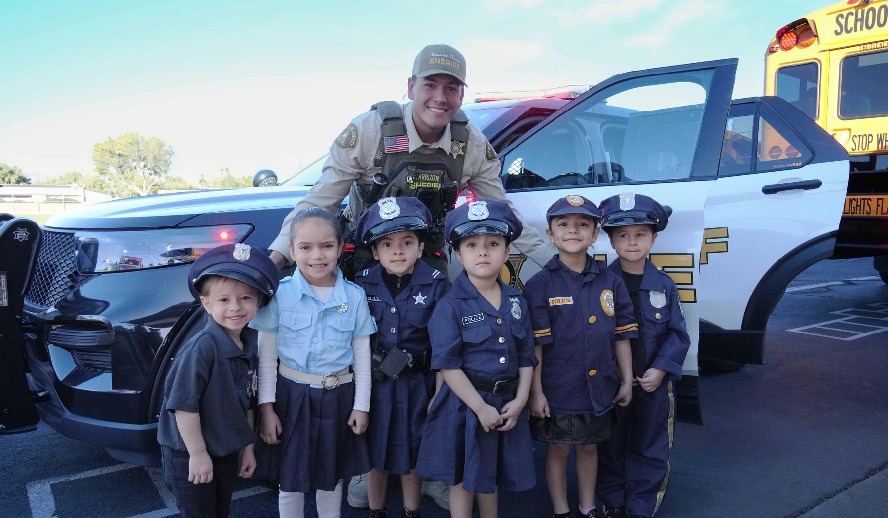 Sheriff officer standing with six young students dressed as police officers