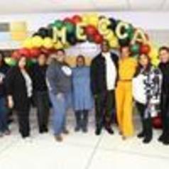 Group of people standing under a colorful balloon arch with the word 'MECCA'.