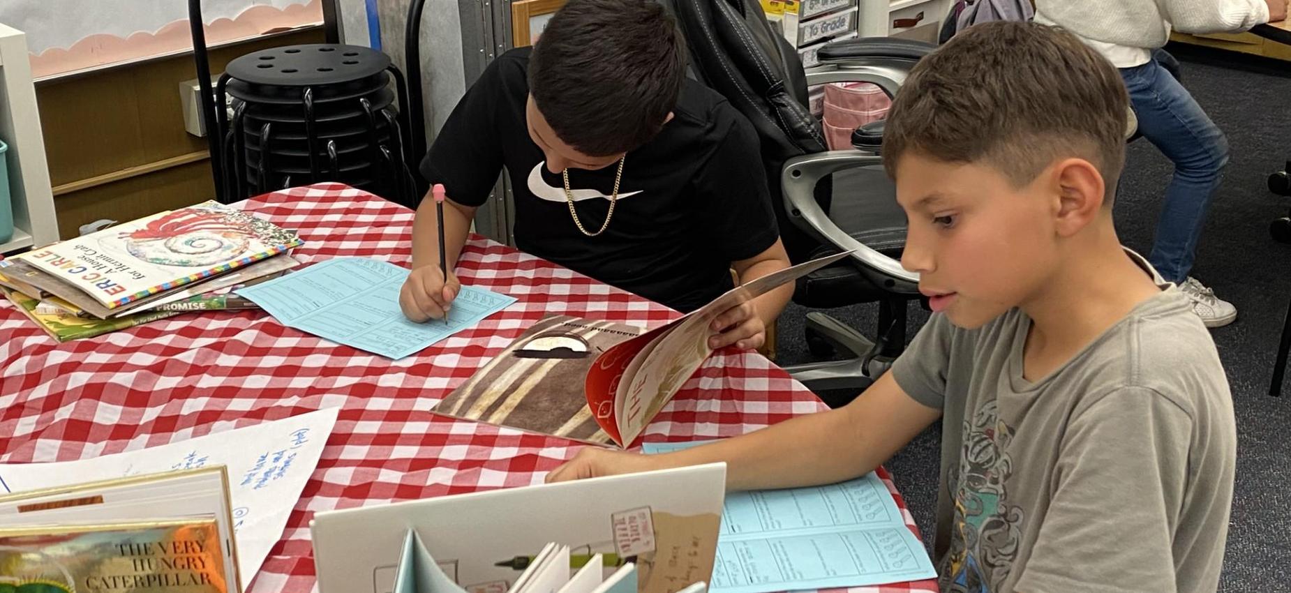 Two boys working on their school assignments at a checkered table.